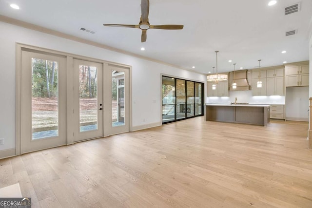 unfurnished living room featuring french doors, sink, crown molding, ceiling fan, and light hardwood / wood-style floors