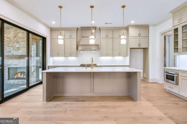 kitchen featuring sink, hanging light fixtures, a kitchen island with sink, stainless steel appliances, and custom range hood