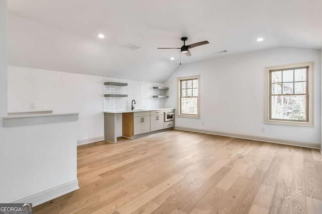 unfurnished living room with lofted ceiling, sink, light hardwood / wood-style flooring, and ceiling fan