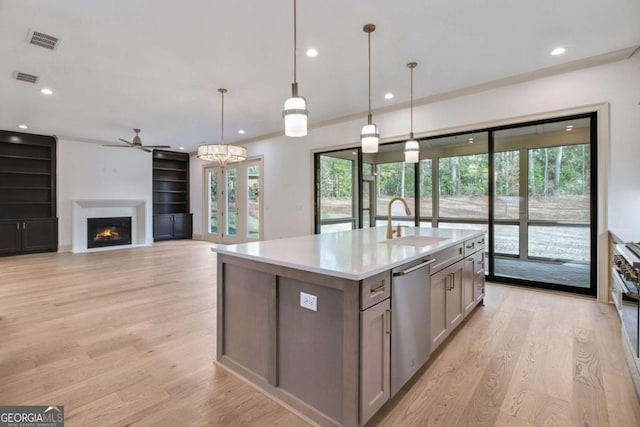 kitchen featuring decorative light fixtures, sink, a kitchen island with sink, stainless steel dishwasher, and light hardwood / wood-style flooring