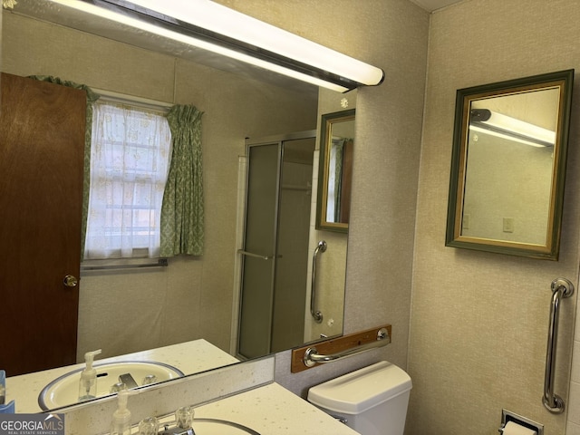 bathroom featuring toilet, a shower with shower door, and sink