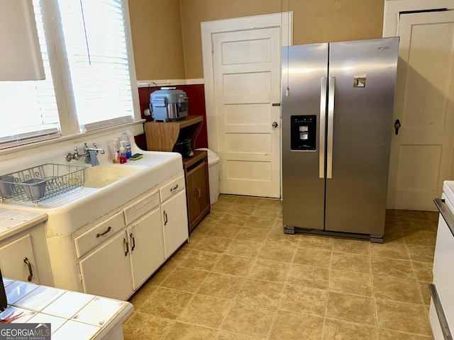 kitchen featuring sink, tile counters, white cabinets, and stainless steel refrigerator with ice dispenser