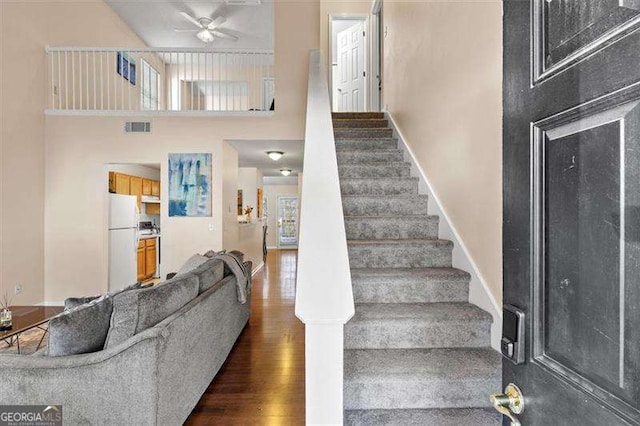 stairs with hardwood / wood-style floors, a towering ceiling, and ceiling fan