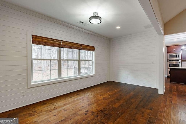 unfurnished room featuring dark wood-type flooring, visible vents, and wood walls