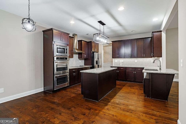 kitchen featuring a center island, stainless steel appliances, hanging light fixtures, a sink, and wall chimney exhaust hood