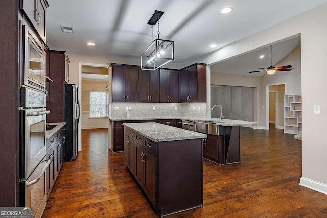 kitchen featuring dark brown cabinetry, appliances with stainless steel finishes, light stone counters, a center island, and pendant lighting