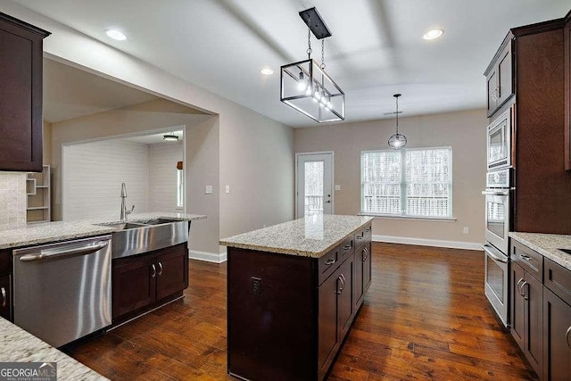 kitchen featuring a kitchen island, appliances with stainless steel finishes, light stone counters, hanging light fixtures, and a sink