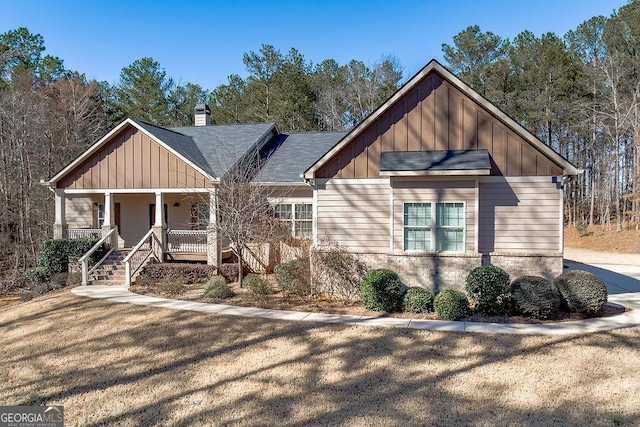 view of front of house featuring roof with shingles, a chimney, covered porch, stairway, and board and batten siding