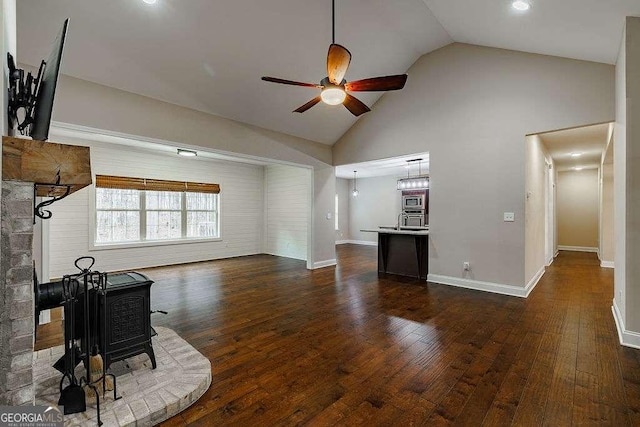 living room with high vaulted ceiling, dark wood finished floors, a wood stove, and a ceiling fan