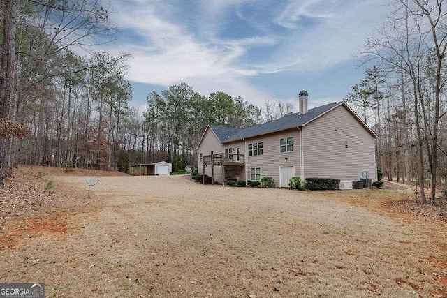 rear view of house with driveway, a chimney, a storage unit, a wooden deck, and an outdoor structure