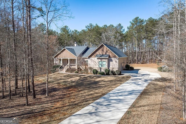 view of front of home featuring a forest view, a chimney, roof with shingles, a porch, and board and batten siding