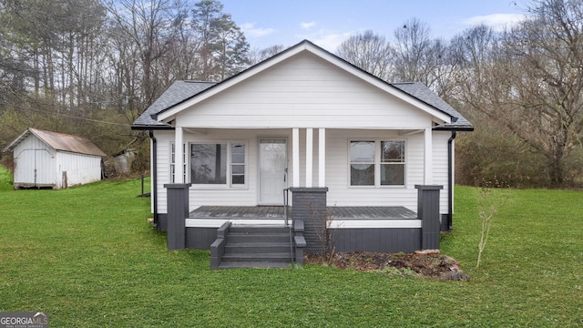 bungalow-style house with covered porch, roof with shingles, a front yard, and an outbuilding