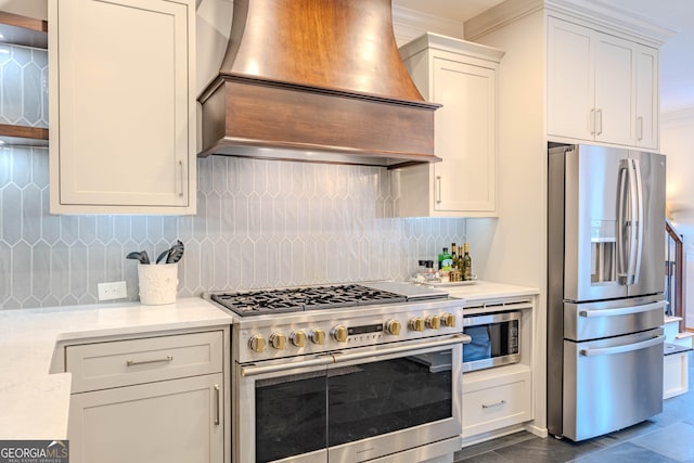 kitchen with appliances with stainless steel finishes, white cabinetry, light stone counters, custom range hood, and decorative backsplash