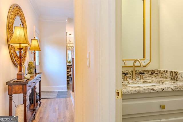 hallway featuring ornamental molding, sink, an inviting chandelier, and light hardwood / wood-style flooring