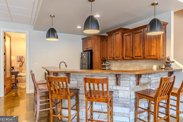 kitchen with hanging light fixtures, decorative backsplash, a breakfast bar, and black fridge