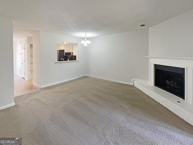 unfurnished living room with a fireplace, carpet floors, a textured ceiling, and a notable chandelier