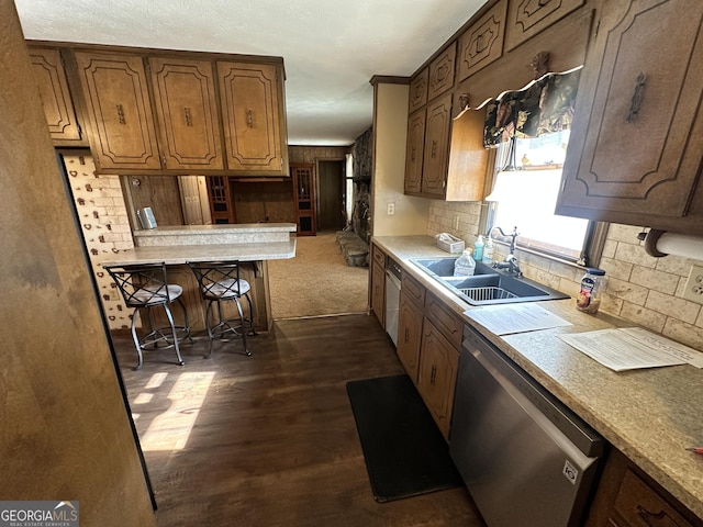 kitchen with dark wood-type flooring, a kitchen bar, sink, dishwasher, and backsplash