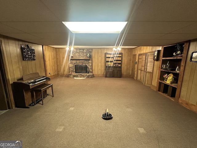 interior space with carpet floors, wooden walls, a paneled ceiling, and a fireplace