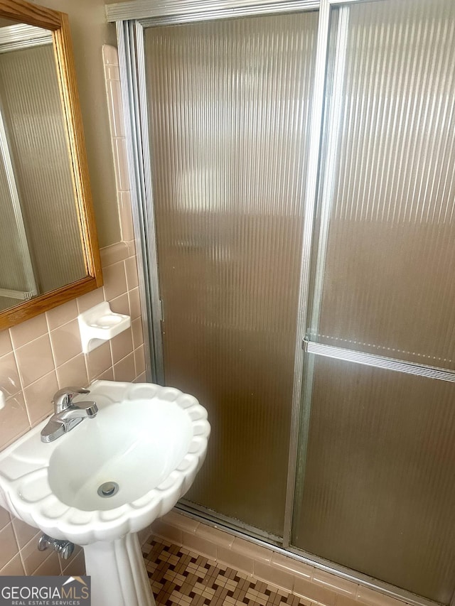 bathroom featuring tasteful backsplash, a shower with shower door, sink, and tile walls