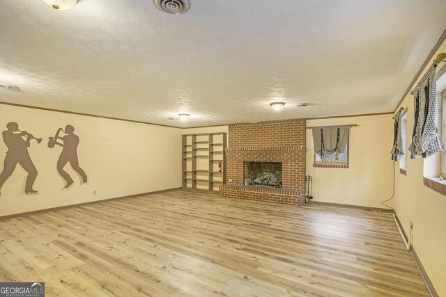 unfurnished living room featuring ornamental molding, light hardwood / wood-style floors, a brick fireplace, and a textured ceiling