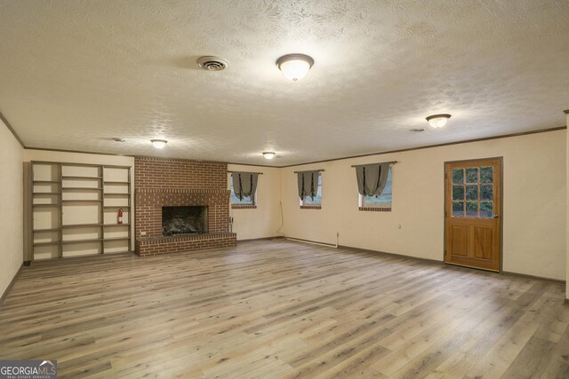 unfurnished living room featuring hardwood / wood-style flooring, crown molding, a textured ceiling, and a fireplace