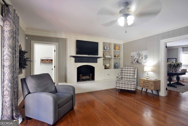 living room featuring dark hardwood / wood-style floors, ceiling fan, crown molding, a brick fireplace, and built in shelves