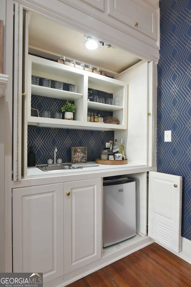 bar with sink, dark wood-type flooring, white cabinets, and stainless steel refrigerator