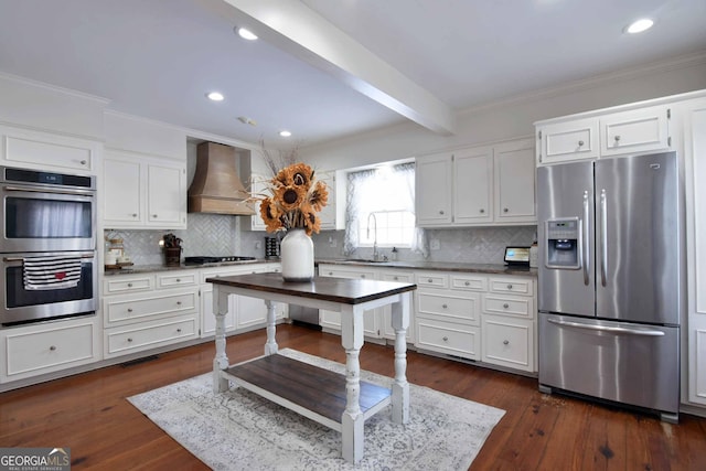 kitchen with dark wood-type flooring, wall chimney exhaust hood, white cabinetry, stainless steel appliances, and beam ceiling