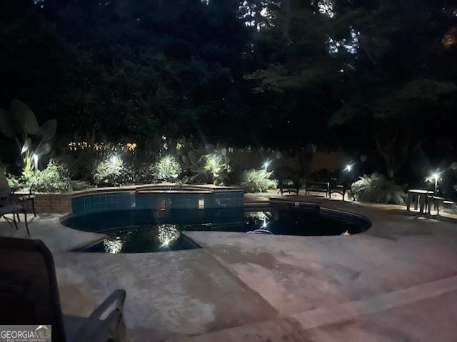 pool at night featuring a patio area and a hot tub