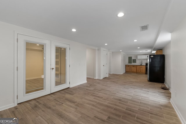 unfurnished living room featuring sink, french doors, and light wood-type flooring