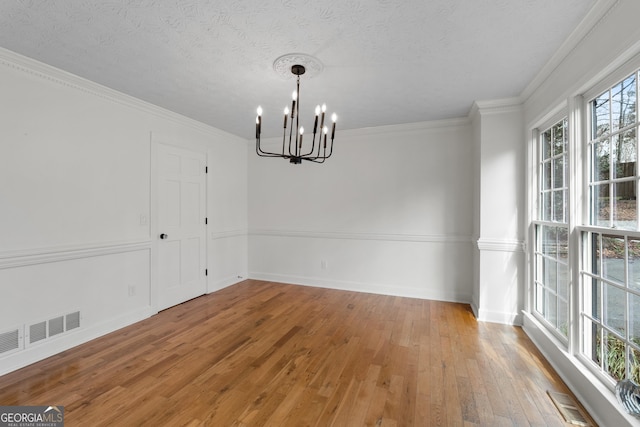 unfurnished dining area featuring crown molding, a notable chandelier, hardwood / wood-style flooring, and a textured ceiling