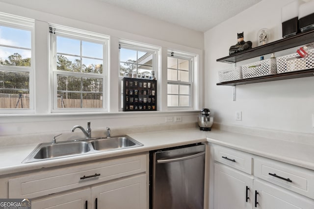 kitchen featuring white cabinetry, sink, stainless steel dishwasher, a healthy amount of sunlight, and a textured ceiling