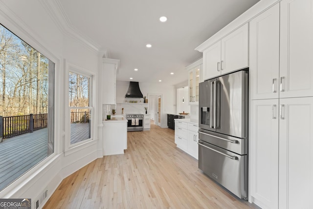 kitchen with premium range hood, white cabinetry, ornamental molding, stainless steel appliances, and light hardwood / wood-style floors