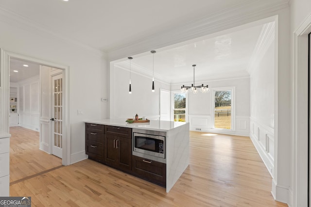 kitchen with pendant lighting, stainless steel microwave, ornamental molding, dark brown cabinets, and light wood-type flooring