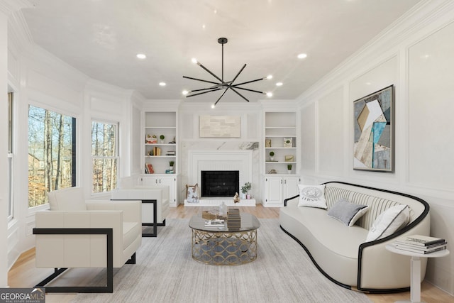 living room featuring built in shelves, ornamental molding, a chandelier, and light hardwood / wood-style floors