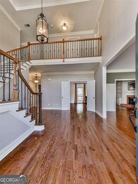 foyer entrance with a notable chandelier, a towering ceiling, ornamental molding, and hardwood / wood-style flooring