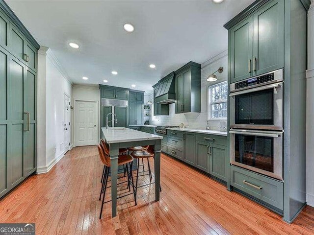 kitchen featuring appliances with stainless steel finishes, backsplash, a kitchen bar, green cabinetry, and light hardwood / wood-style flooring