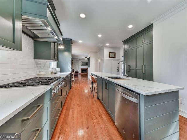 kitchen featuring sink, light stone counters, light hardwood / wood-style flooring, a large island with sink, and appliances with stainless steel finishes