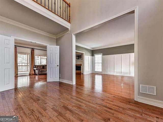 unfurnished living room with hardwood / wood-style flooring, ornamental molding, a towering ceiling, and a wealth of natural light