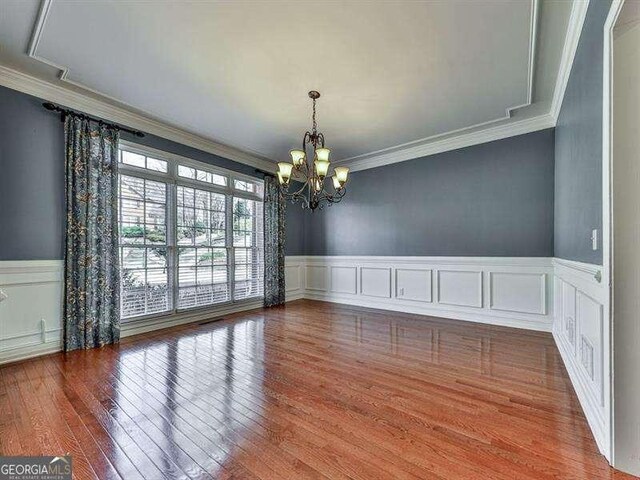 unfurnished dining area with hardwood / wood-style floors, crown molding, and a chandelier