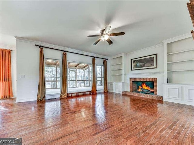 unfurnished living room featuring crown molding, wood-type flooring, a fireplace, and built in features