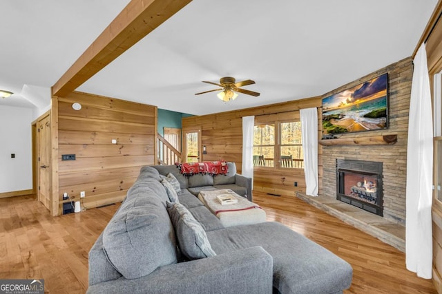 living room with ceiling fan, wooden walls, a fireplace, and light wood-type flooring