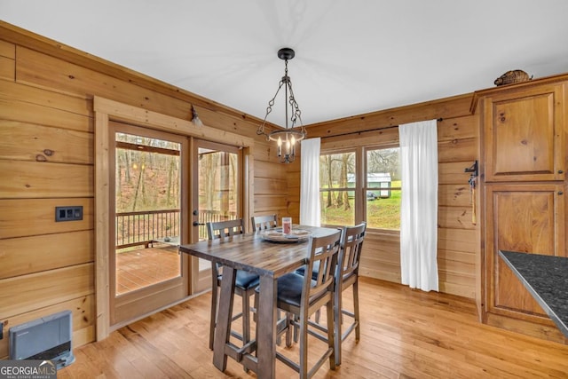 dining area featuring a notable chandelier, wood walls, and light wood-type flooring