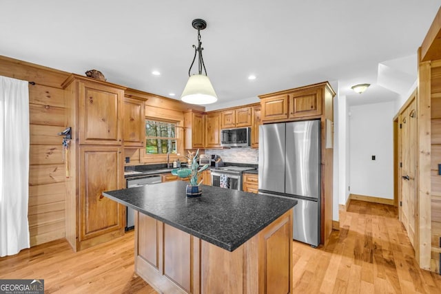 kitchen featuring a kitchen island, appliances with stainless steel finishes, pendant lighting, backsplash, and light hardwood / wood-style flooring