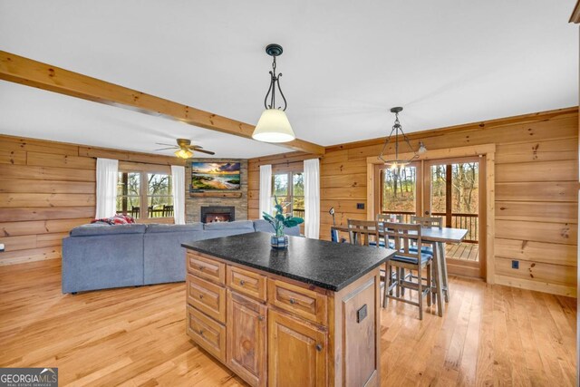 kitchen with a kitchen island, wood walls, beamed ceiling, hanging light fixtures, and light wood-type flooring