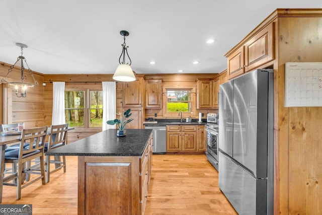 kitchen with appliances with stainless steel finishes, sink, hanging light fixtures, a center island, and light hardwood / wood-style floors