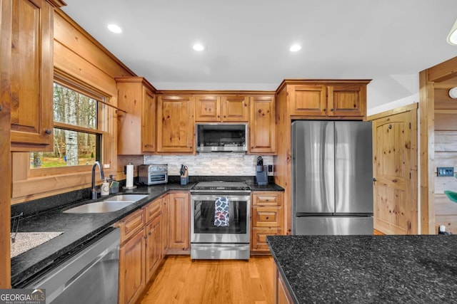 kitchen featuring sink, appliances with stainless steel finishes, dark stone counters, light hardwood / wood-style floors, and backsplash