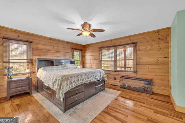 bedroom with light hardwood / wood-style floors, multiple windows, and wood walls