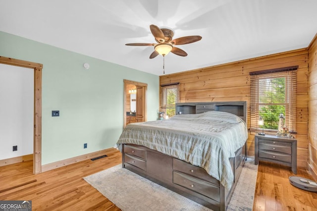 bedroom with ceiling fan, wooden walls, multiple windows, and light wood-type flooring