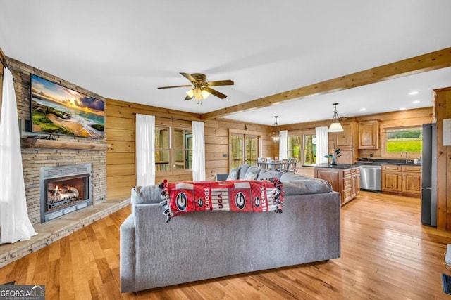 living room with beam ceiling, a stone fireplace, wooden walls, and light wood-type flooring